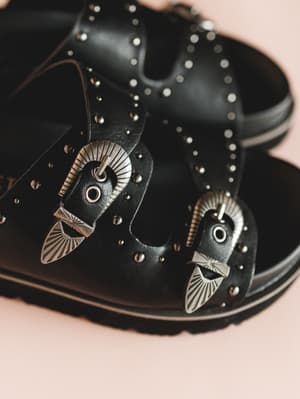 Black leather shoes with decorative metal accents on a pink background