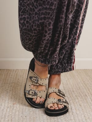 Person wearing leopard print pants and beige sandals with black straps on a neutral background