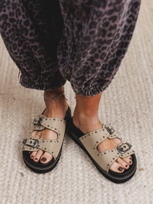 Beige sandals with black soles worn with leopard print pants on a neutral background