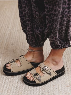 Beige sandals with buckles worn with leopard print pants on a neutral background