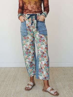 A mixed-media pant that can't quite decide if it's denim or a wildflower field — and that's exactly the point. Floral tapestry panels meet medium-wash denim with a navy drawstring waist, styled with a sheer rust top, beaded bracelets, and white buckl