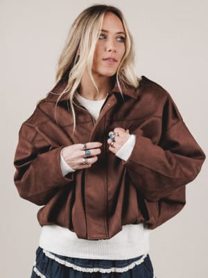 Woman wearing a brown jacket over a white shirt with a beige background