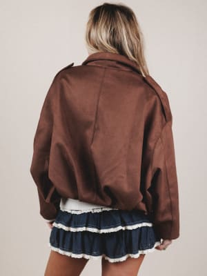 Person wearing a brown jacket and a blue skirt with white trim on a plain background