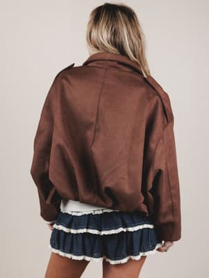 Person wearing a brown jacket and a blue skirt with white trim on a plain background