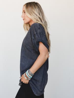 A relaxed side-profile shot of a washed charcoal graphic tee styled with stacked boho beaded bracelets — the kind of effortless outfit that looks like it took zero effort but absolutely did not.