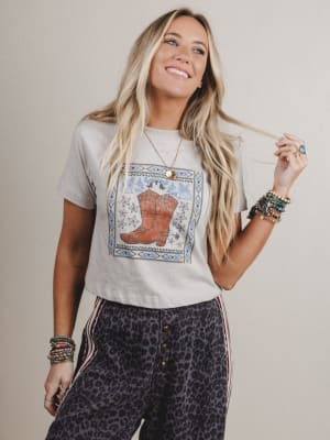Woman wearing a graphic t-shirt with a boot design and leopard print pants against a plain background