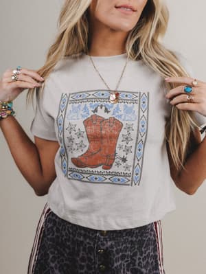 Person wearing a white t-shirt with a graphic of a cowboy boot and decorative elements.
