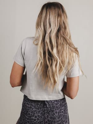 Person with long blonde hair wearing a light gray t-shirt and patterned pants against a neutral background