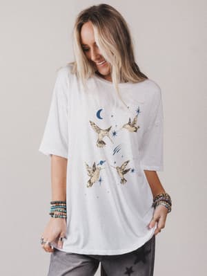 Woman wearing a white t-shirt with bird and moon designs on a plain background