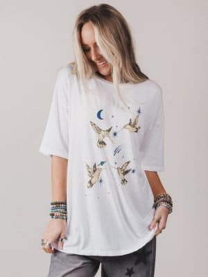 Woman wearing a white t-shirt with bird and moon designs on a plain background