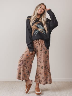 Woman wearing a black sweatshirt with a graphic design and patterned pants against a plain background