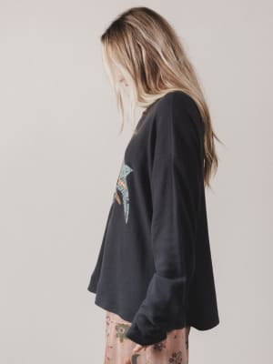 Person wearing a black oversized sweatshirt with a colorful graphic on a plain background