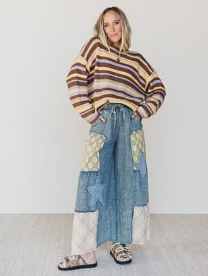 Person wearing a striped sweater and patchwork denim pants on a white background