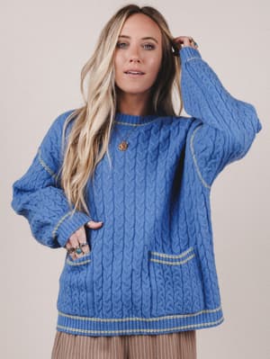 Woman wearing a blue cable knit sweater against a plain background