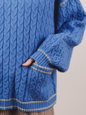 Close-up of a blue cable knit sweater with a neutral background