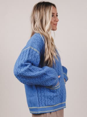 Woman wearing a blue cable knit sweater against a plain background