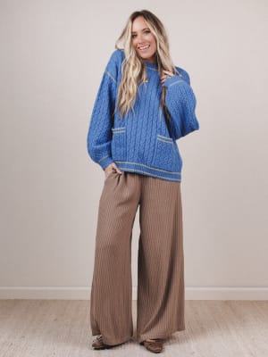 Woman wearing a blue knitted sweater and brown wide-leg pants against a plain background