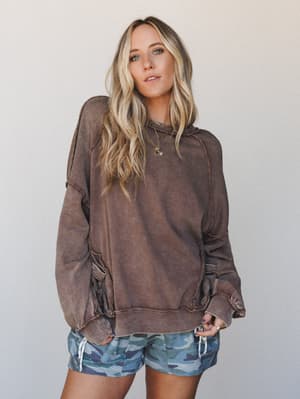 A relaxed, lived-in mineral-washed sweatshirt in a warm cacao brown is paired with blue camo shorts — the kind of effortless combo that looks like it just happened but totally didn't.