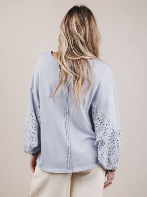 Person wearing a light blue blouse with sheer sleeves against a beige background