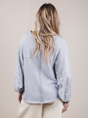 Person wearing a light blue blouse with sheer sleeves against a beige background