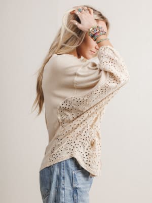 Woman wearing a beige sweater with cut-out details and blue jeans on a plain background
