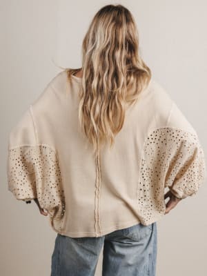 Person wearing a beige sweater with sheer sleeves against a plain background