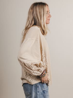 Woman wearing a beige blouse with lace details and blue jeans against a plain background