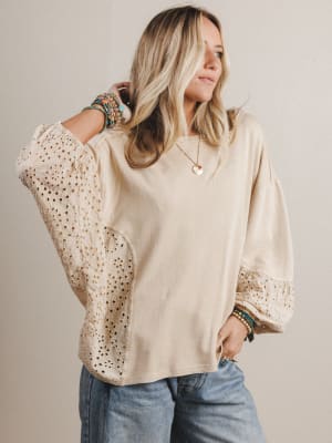 Woman wearing a beige blouse with lace details on a plain background