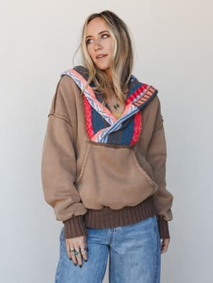 A lived-in mocha hoodie with a bold woven serape-style collar gets styled with light wash wide-leg jeans and layered silver jewelry — the kind of outfit that feels intentional without trying too hard.