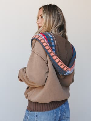 Shot from behind with a glance back over the shoulder, this layered look pairs an oversized mocha hoodie with a fair isle knit vest, the kind of cozy, collected combination that feels equally at home on a coffee run or a weekend road trip.