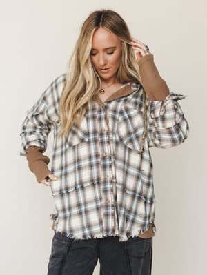An oversized plaid shacket with raw-edge fringe detailing layered over a mocha waffle-knit top, styled with charcoal cargo pants — the kind of effortless fall outfit that looks like it came together in two minutes but actually took zero thought becau