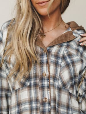 A close-up torso shot of a plaid flannel jacket in warm mocha and navy tones, layered over a camel waffle-knit collar — the kind of piece that looks like it's been lived in for years and still gets reached for first.