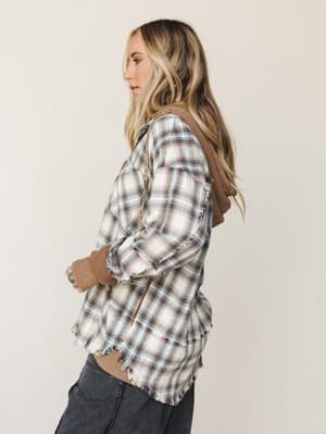 A side-profile shot of a plaid flannel jacket with a knit hoodie underlay and raw frayed hem — the kind of piece that looks like you grabbed it on the way out the door and somehow nailed it.