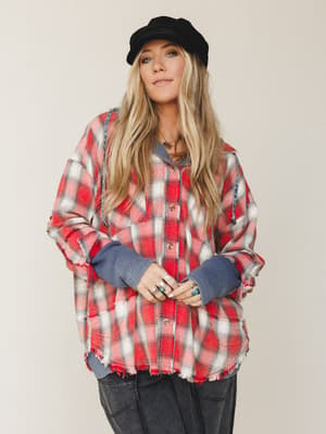 An oversized plaid flannel jacket with raw-edge hem and contrast waffle-knit cuffs and hood, styled with dark cargo pants and a black newsboy cap — the kind of outfit that looks like you grabbed it off a chair and somehow nailed it.