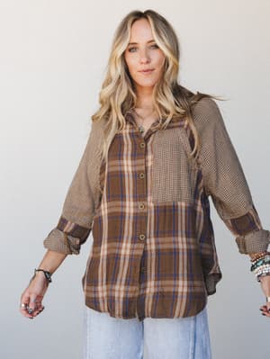 A mixed-print button-down shirt in warm brown plaid and mini houndstooth panels styled with light wash wide-leg jeans and layered boho jewelry — the kind of top that looks like it's been in someone's wardrobe forever, in the best way.