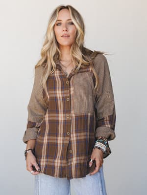 A mixed-print button-down shirt in warm brown plaid and mini check panels gives this look a lived-in, collected feel — styled with stacked bracelets and wide-leg jeans for that effortless everyday energy.