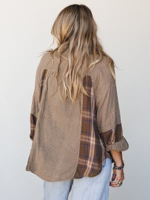 Shot from the back, this mixed-print button-down in warm camel and brown layers a mini gingham with a plaid panel — the kind of shirt that looks like it's been loved for years and styled with light-wash jeans and stacked bracelets for exactly the rig
