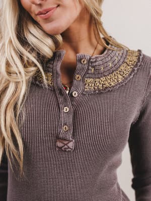 Close-up of a woman wearing a textured brown sweater with a decorative neckline.