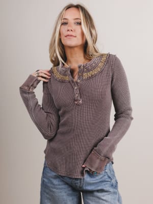 Woman wearing a brown long-sleeve top with embroidered collar against a plain background