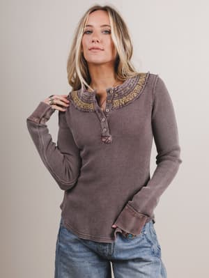Woman wearing a brown long-sleeve top with embroidered collar against a plain background
