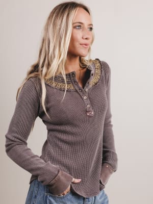 Woman wearing a brown long-sleeve top with decorative neckline against a plain background
