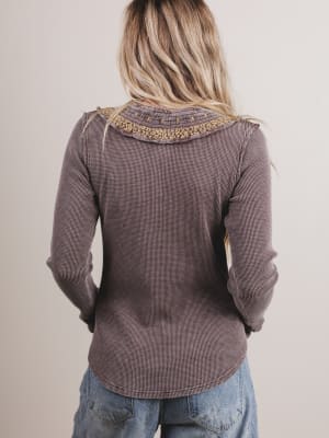 Person wearing a brown long-sleeve top with lace trim on a beige background