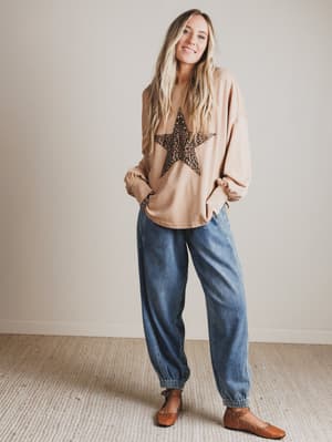 Woman wearing a blush-colored sweater with a star design and blue jeans standing against a plain background