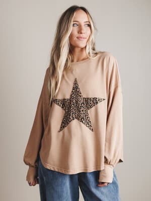 Woman wearing a blush-colored long-sleeve top with a leopard print star design on a plain background