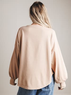 Back view of woman wearing a blush-colored oversized sweater with balloon sleeves on a plain background