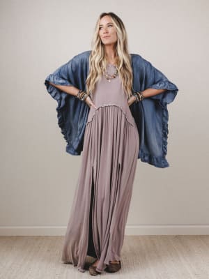 Woman wearing a long mauve dress with a denim cover-up against a plain background
