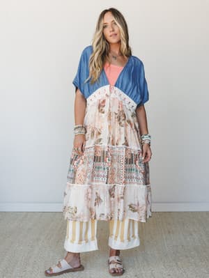 A layered boho look featuring a washed denim kimono with crochet trim over a floral and geometric mixed-print midi dress and wide-leg striped pants — free-spirited and effortlessly put-together, like she packed it all in one carry-on and made it work