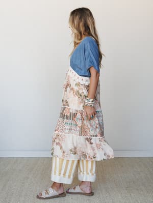 A side-profile shot of a model layered in a mixed-print floral and geometric kimono with crochet trim over a chambray tee, styled with wide-leg striped pants and neutral buckle sandals — the kind of effortlessly collected outfit that looks like it ca