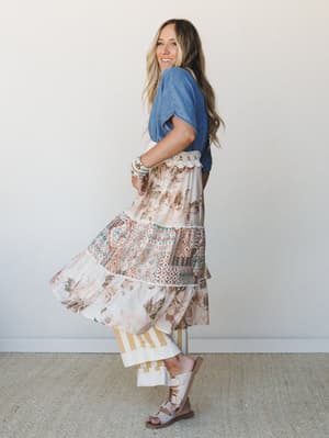 A model twirls in a washed denim kimono layered over a floral and aztec-print tiered maxi skirt, styled with stacked bracelets and buckle sandals — the kind of effortless boho mix that looks like it came together on instinct.