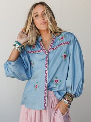 A relaxed chambray blouse with floral embroidery and zigzag trim styling paired with a blush midi skirt, stacked beaded bracelets layered on both wrists — the kind of outfit that looks effortless but clearly had a thought behind it.